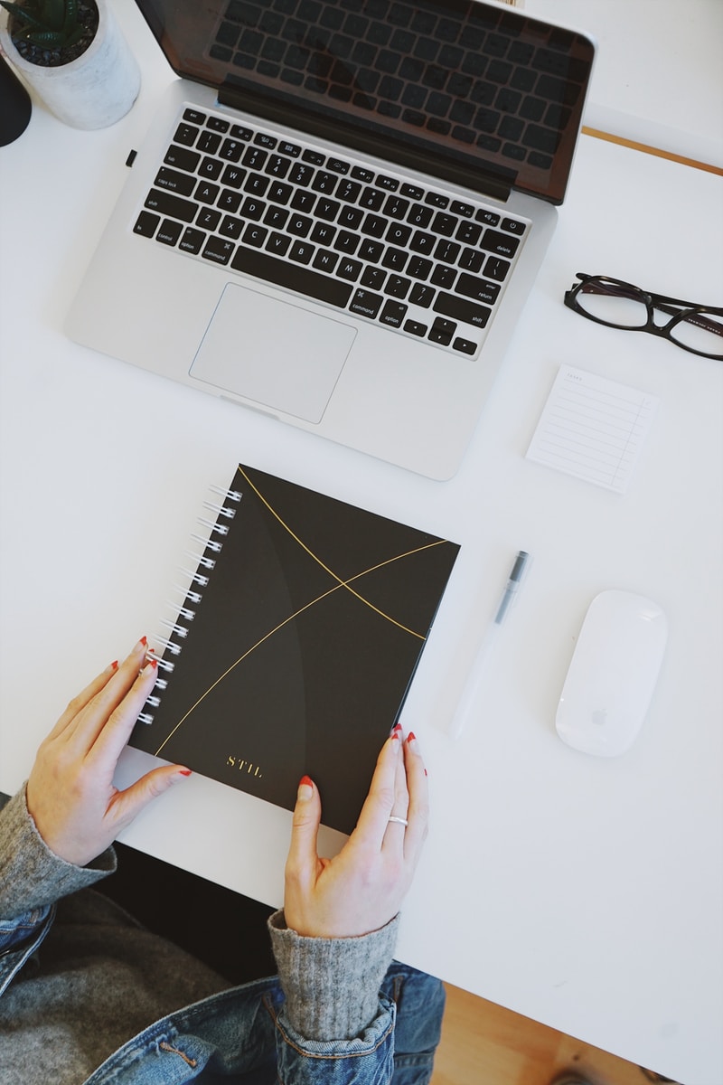 person holding notebook near laptop